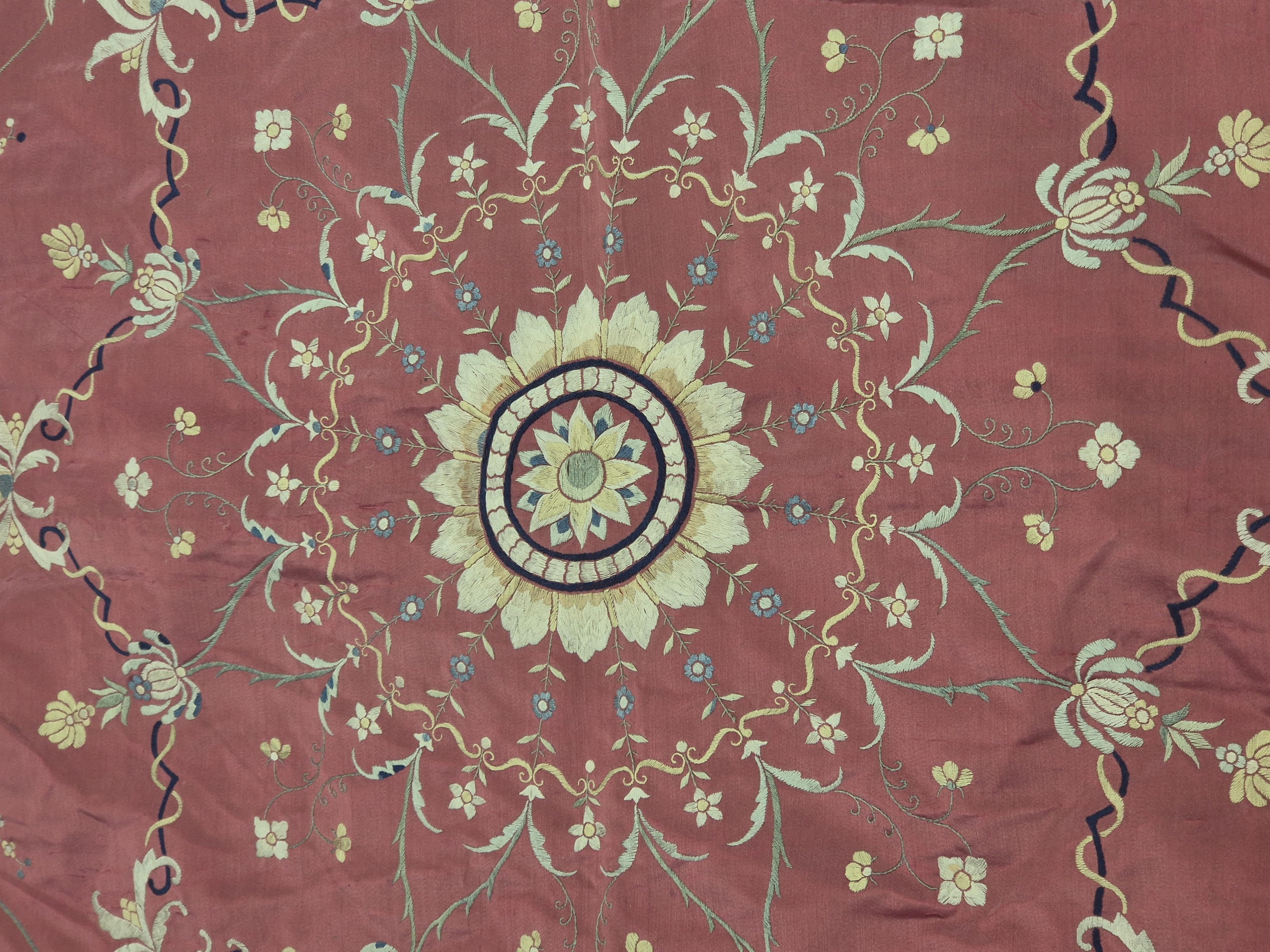 A Chinese 19th century Qing Dynasty crimson red silk embroidered hanging. Embroidered with sprays and swags of flowers and foliage, depicting prosperity and fortune, around a central stylistic sun motif, depicting perfec